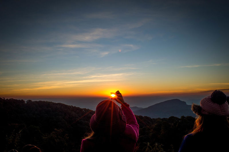 Optical illusion woman holding sun at sunset