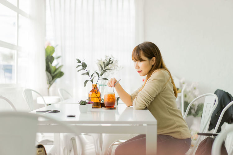 Side view of young woman having drink while sitting at home