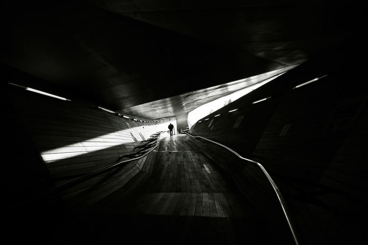 Rear view of silhouette man walking on road in tunnel