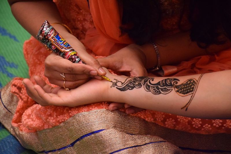 Midsection of female artist applying henna tattoo on woman during wedding