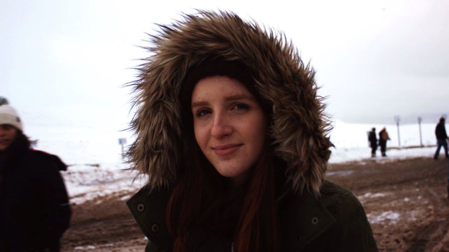 Portrait of young woman wearing warm clothes while standing on snow covered field