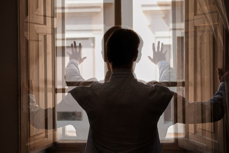 Double exposure of man looking through window at home