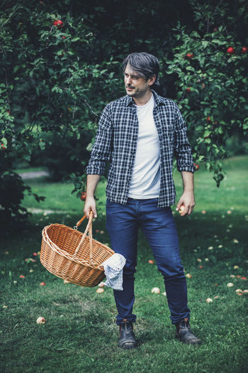 Full length of man carrying wicker basket at apple orchard