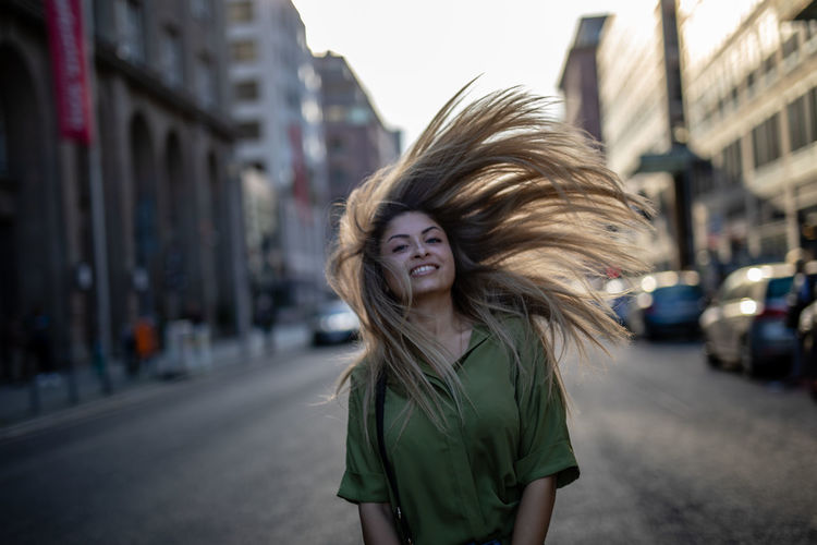 Portrait of young woman tossing hair while standing on city street