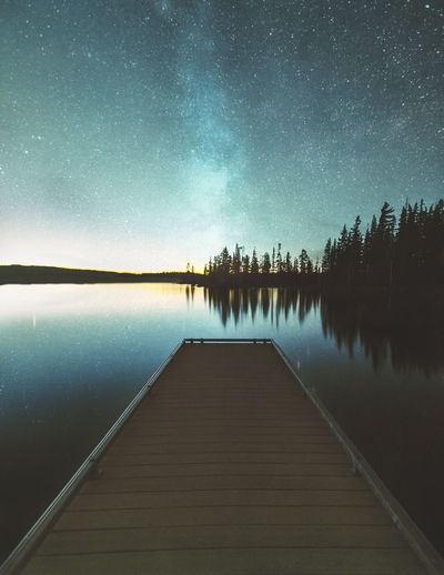 Pier amidst lake against sky at night