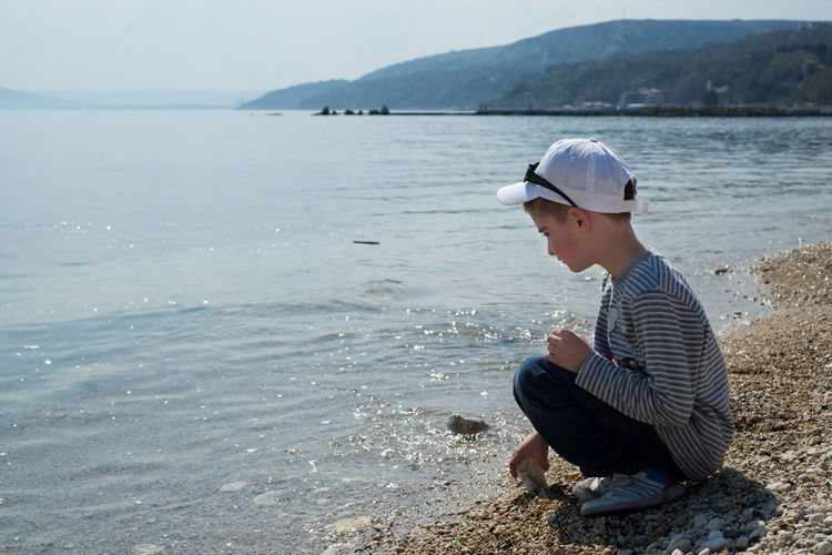 Side view of boy crouching on shore at beach during summer