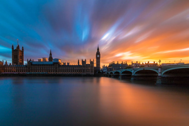 Bridge over river by big ben against cloudy sky during sunset