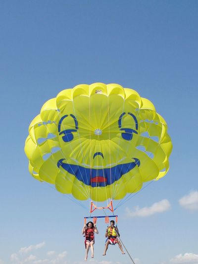 Low angle view of people parasailing against sky