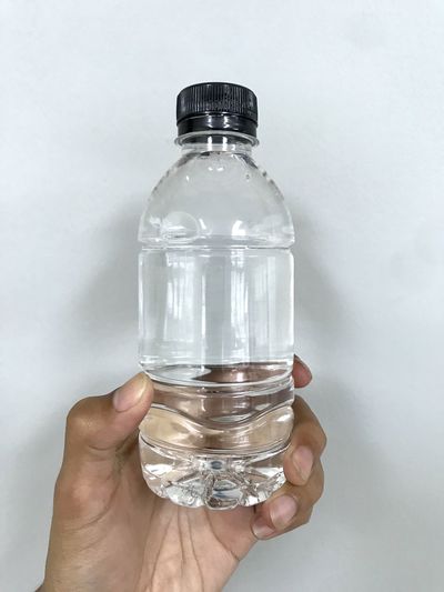 Close-up of hand holding glass bottle against white background