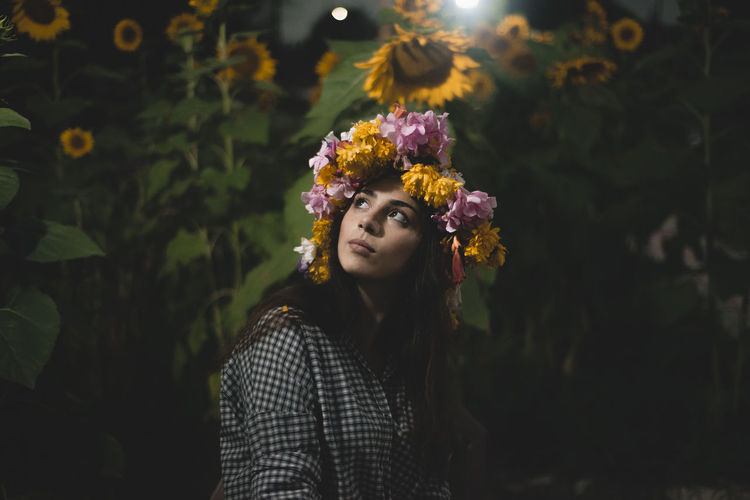 Side view of thoughtful woman wearing flowers at farm during night
