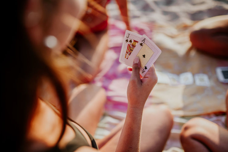 High angle back view of unrecognizable young woman holding cards while playing game with friends on beach
