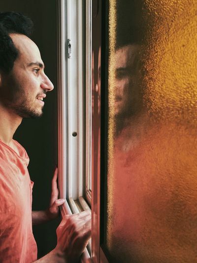 Profile view of man looking through window at home