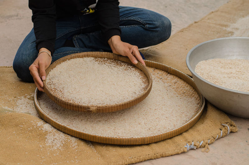 Low section of person sieving rice in wicker plate
