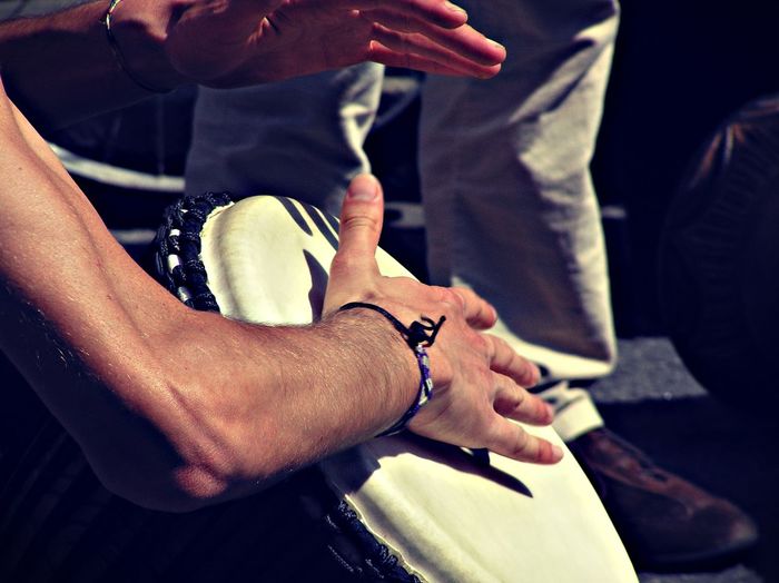 Cropped hands of man playing drum on footpath during sunny day