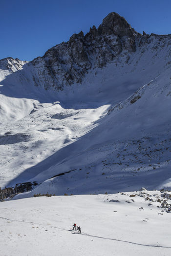 Skiers skin below a jagged peak in the san juan mountains of colorado.