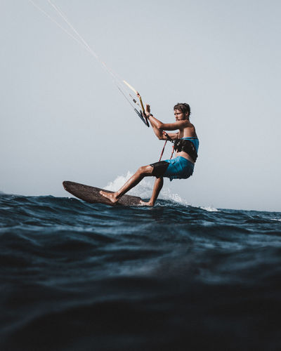 Side view of man kiteboarding in sea against clear sky