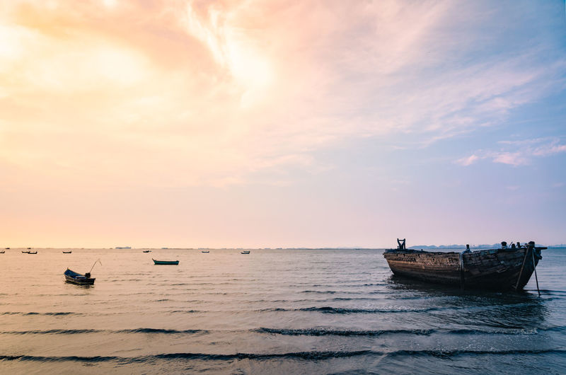 Boats moored in sea against sky during sunset