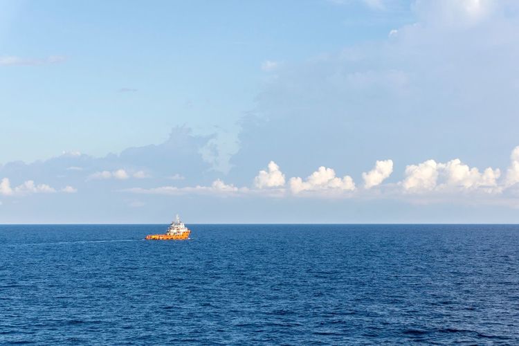 Ship sailing in sea against cloudy sky