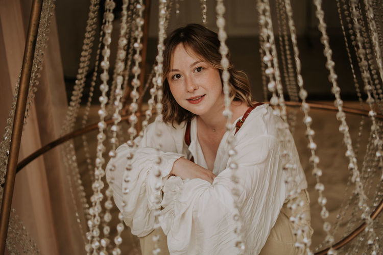 Young female in victorian shirt sitting in giant crystal chandelier and smile