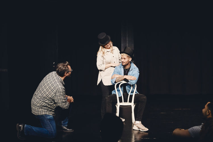 Instructor looking at man and woman wearing hat rehearsing on stage