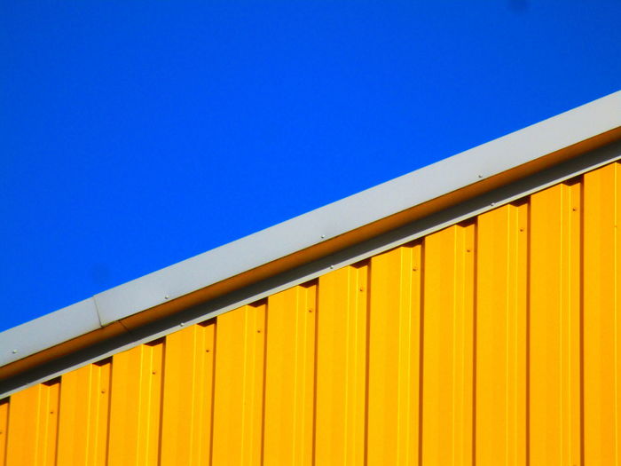 Low angle view of yellow metallic structure against blue sky
