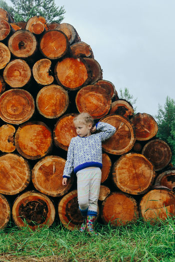 Rustic style, a girl in casual clothes sits on a bench against the background of a woodpile