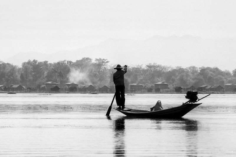 Fisherman standing on boat in lake against sky