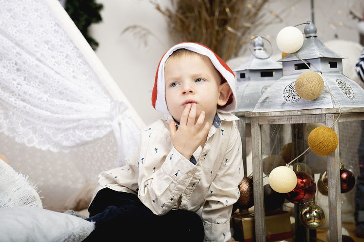 Portrait of a cute child boy kid wearing a christmas hat sitting among the holiday decorations