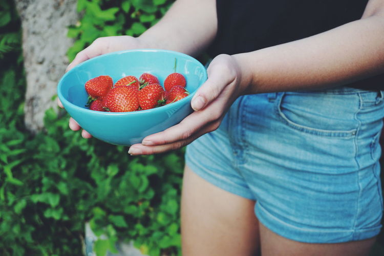 Midsection of woman holding strawberries in bowl
