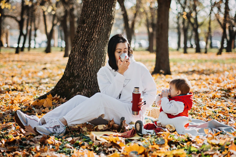 Happy family mother and little toddler baby daughter having autumn picnic with red thermos and cup