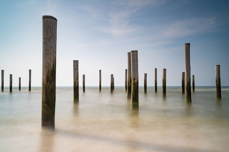 Wooden posts on pier in sea against sky
