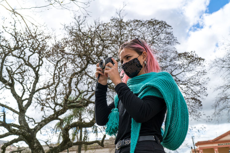 Young woman wearing flu mask photographing in city