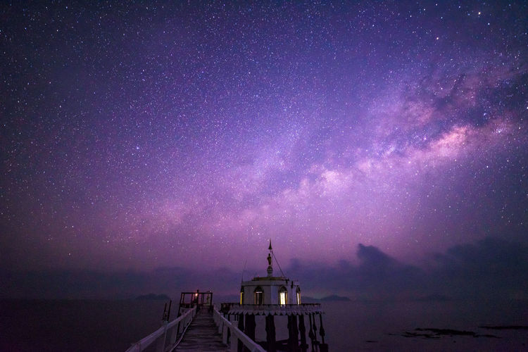 Pier over sea against milky way at night