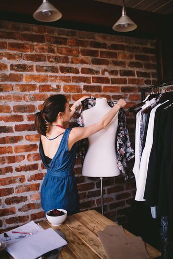 Female fashion designer arranging clothes on mannequin against brick wall