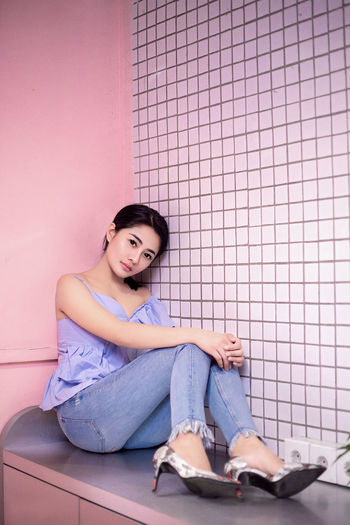 Portrait of young woman sitting on floor against wall
