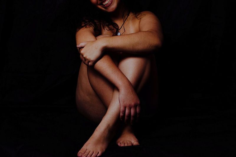 Midsection of young woman sitting against black background