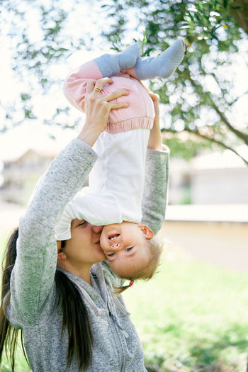 Side view of woman holding baby upside down outdoors