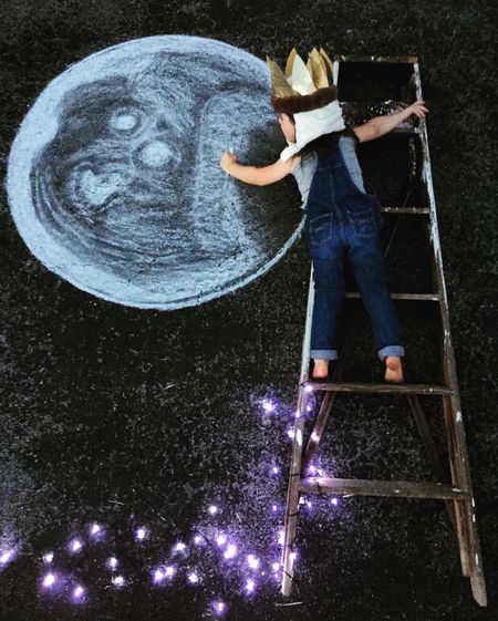 High angle view of girl lying on ladder while drawing moon on footpath