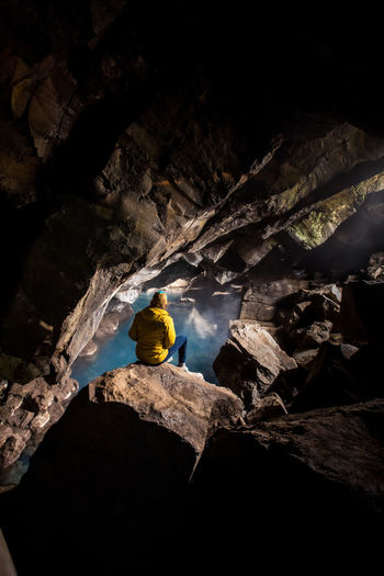 Woman sitting in front of thermal pool in cave