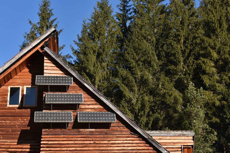 Low angle view of wooden house with solar panels amidst trees against sky