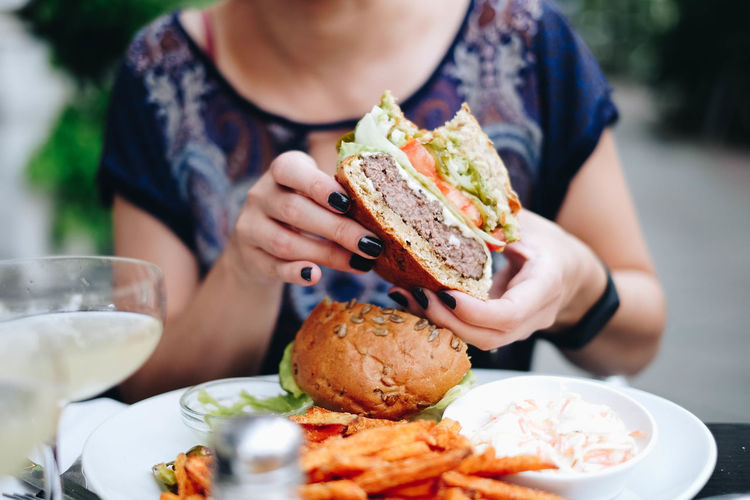 Midsection of woman holding having burger at restaurant