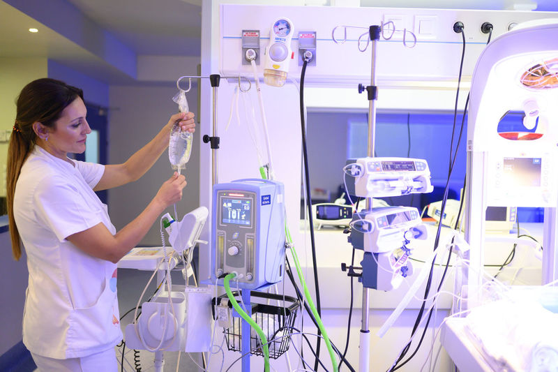 Side view of medical practitioner adjusting a bag of iv saline near modern monitor while working in hospital