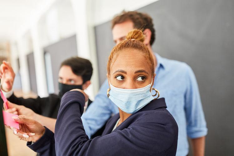 Businesswoman wearing mask looking away while standing with colleagues