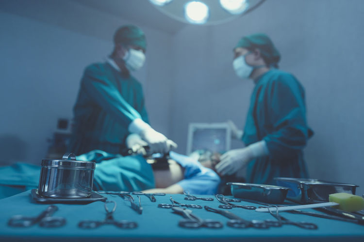 While performing medical surgery inside the operating room, a doctor and nurse use a defibrillator .