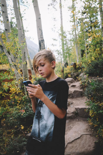 Tween boy checks phone while on a hike in colorado.