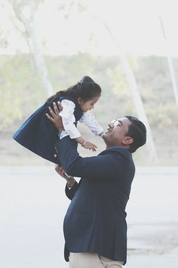 Side view of father carrying daughter while standing outdoors