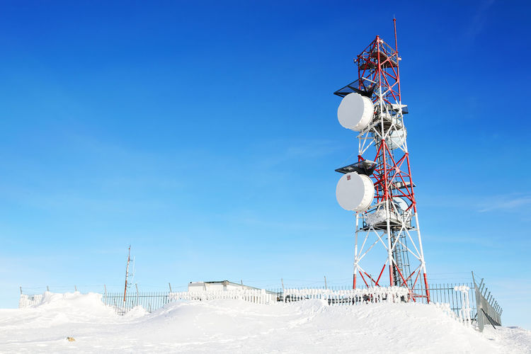 Low angle view of communication tower on snow field against blue sky