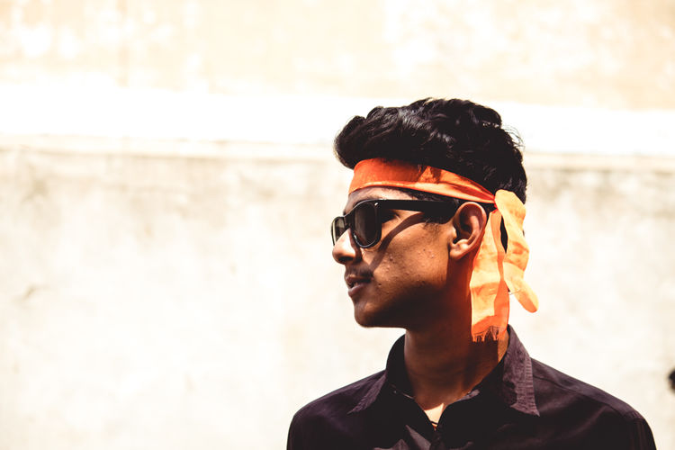 Young man wearing orange bandana looking away while standing outdoors
