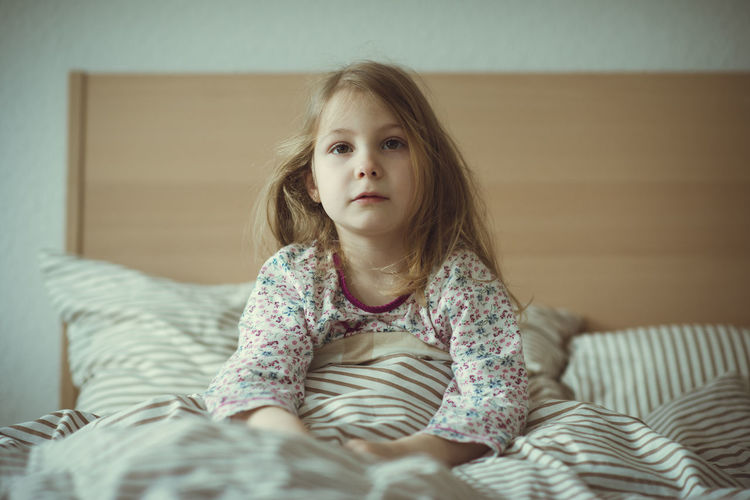 Portrait of cute girl sitting on bed at home