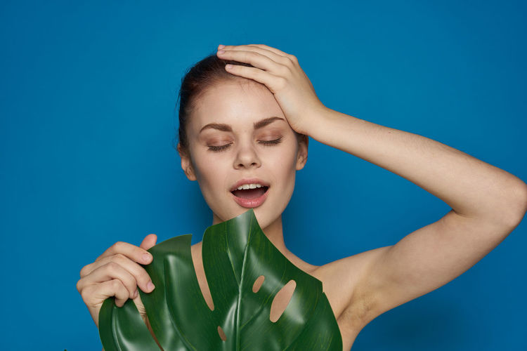 Close-up of young woman holding leaf against blue background